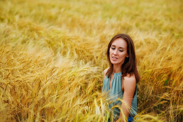 Portret uśmiechniętej kobiety siedzącej na polu pszenicy. Krajobraz letni obszarów wiejskich - Zdjęcie, obraz