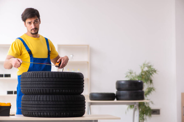 Jovem garagista do sexo masculino com pneu na oficina - Foto, Imagem
