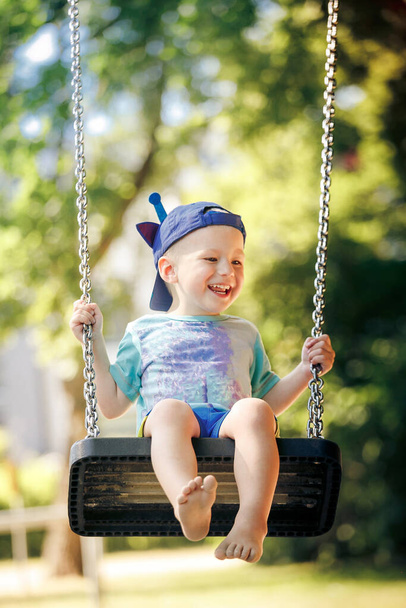 Μικρό αγόρι που διασκεδάζει στην αλυσιδωτή κούνια στην παιδική χαρά - Φωτογραφία, εικόνα