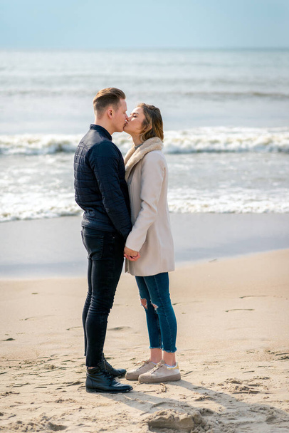 Young couple kissing in love outdoor.Stunning sensual outdoor portrait of young stylish fashion couple posing in spring,autumn sea background. - Photo, Image