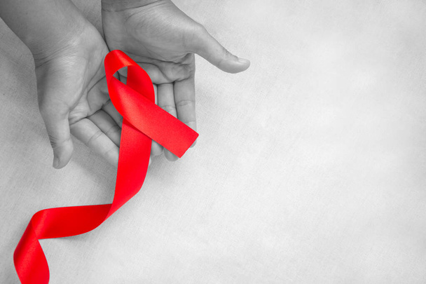 Χέρι κρατώντας κόκκινη κορδέλα σε λευκό φόντο με χώρο αντιγραφής, την αλληλεγγύη των ανθρώπων που ζουν με τον HIV, το σύμβολο του AIDS, και για την ευαισθητοποίηση και την πρόληψη της χρήσης ναρκωτικών και της οδήγησης υπό την επήρεια αλκοόλ. Έννοια υγείας - Φωτογραφία, εικόνα