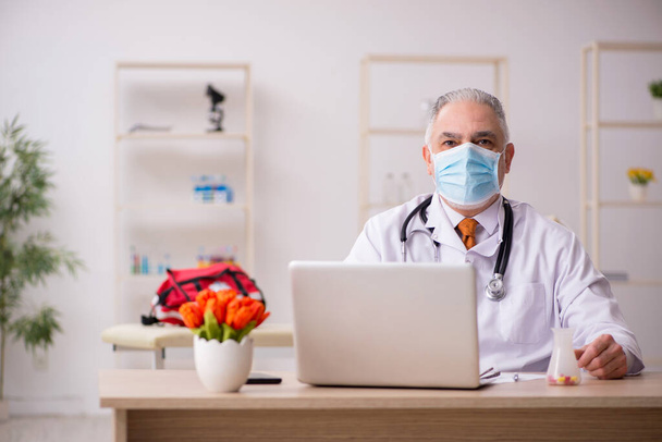 Старый врач-мужчина, работающий в клинике во время пандемии - Фото, изображение