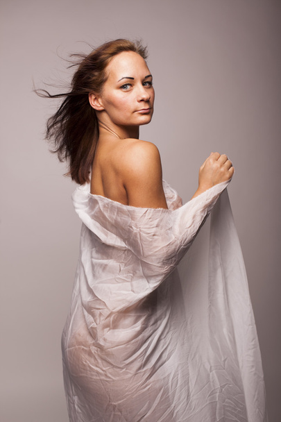 Sexy brunette woman with perfect body covered with white transparent textile on gray isolated background - 写真・画像