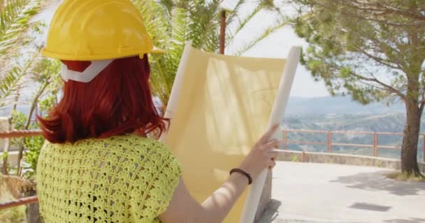Outdoor footage of beauty Italian architect in yellow helmet. Young woman with rolled blueprints in construction side at daytime  - Metraje, vídeo
