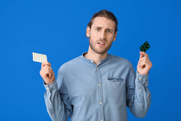 Confused young man with pills on color background - Foto, imagen
