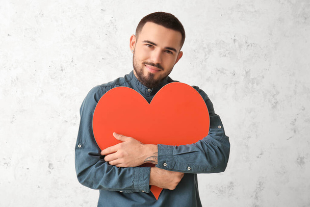 Junger Mann umarmt rotes Herz auf hellem Hintergrund - Foto, Bild