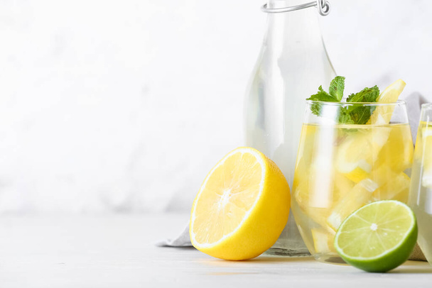 Bottle and glass of tasty cold lemonade on light background, closeup - Foto, afbeelding