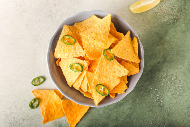 Bowl with tasty nachos, chili pepper and lime on color background - Zdjęcie, obraz