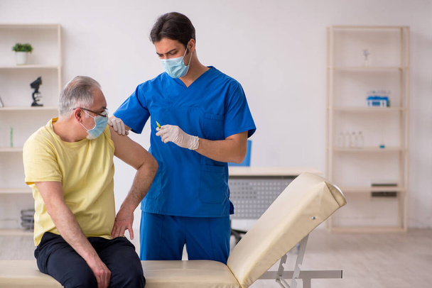 Stary pacjent męski widząc młodego lekarza płci męskiej w zagładzie szczepień - Zdjęcie, obraz