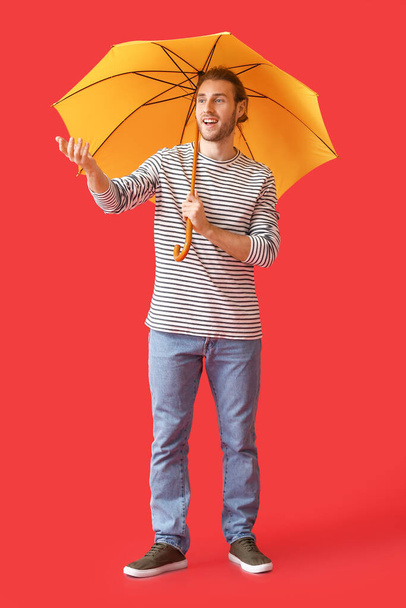 Красивый молодой человек с зонтиком на цветном фоне - Фото, изображение
