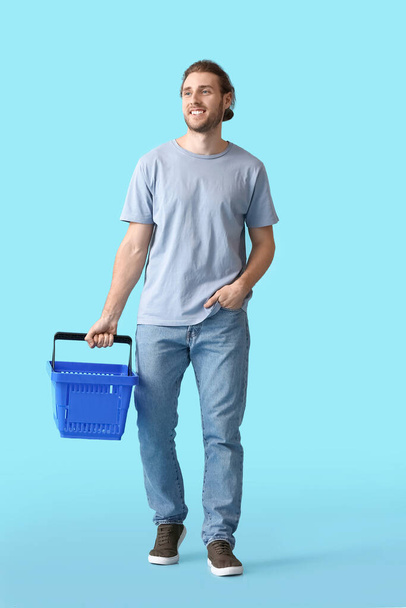 Young man with empty shopping basket on color background - Valokuva, kuva