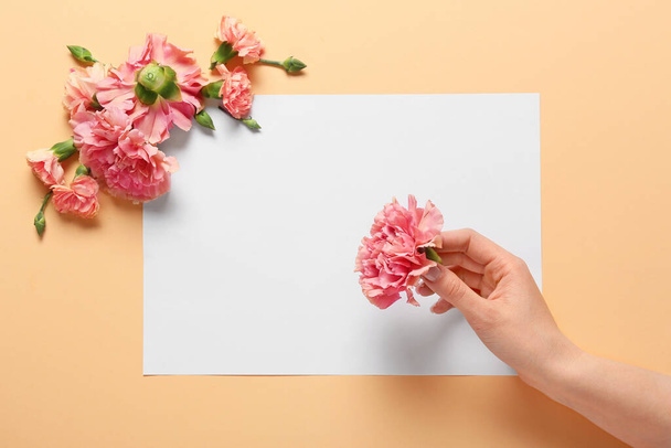 Female hand with beautiful carnation flowers and blank card on color background - Фото, изображение