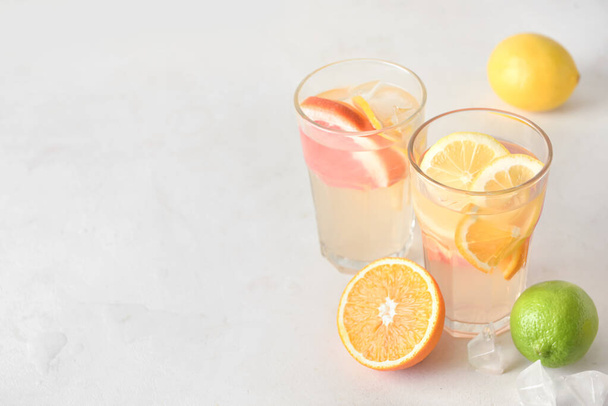 Glasses of tasty cold lemonade and citrus fruits on light background - Фото, изображение