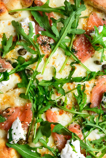 Pizza with mozzarella, salmon slices, fresh arugula. Pizza extreme close up, texture of pizza. Italian cuisine concept, traditional pizza recipe. - Фото, изображение