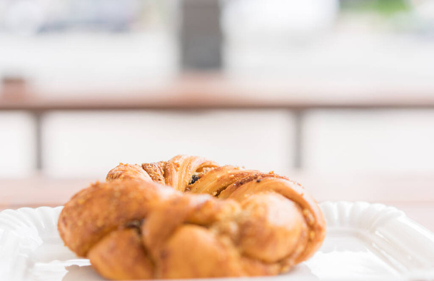 El bagel recién horneado en el plato blanco plano en la panadería a la mesa al aire libre. Enfoque selectivo. Hermoso bokeh - Foto, imagen