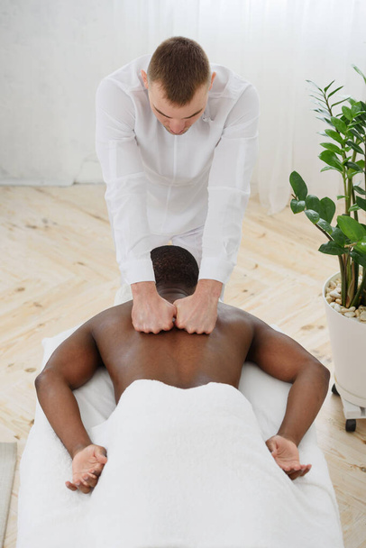 African american man having back massage in spa, white background. Copy space - Foto, Bild