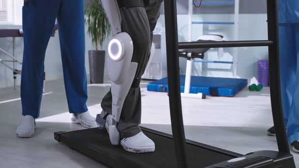 Man in exoskeleton walking on treadmill near rehabilitation therapists - Photo, Image