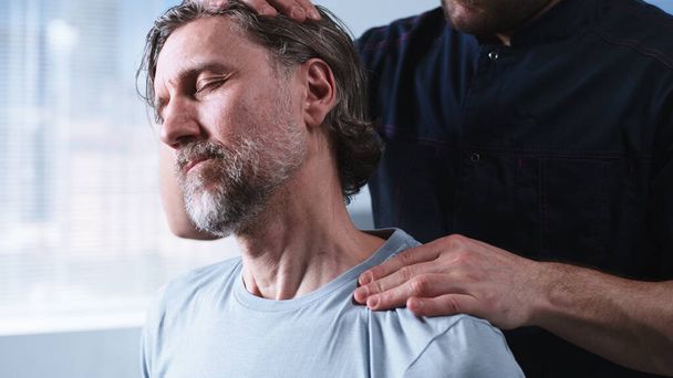 Севотерапевт растягивает шею мужчине средних лет - Фото, изображение