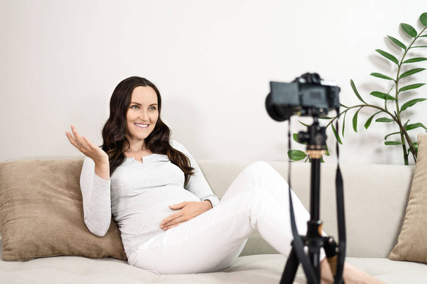 вагітна жінка сидить на дивані веде канал, знімається на відеокамеру, блогер, мама на материнській відпустці, фрілансер
 - Фото, зображення