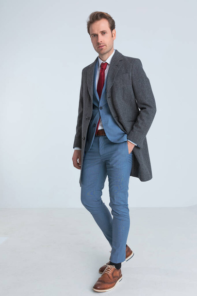 елегантний модний бізнесмен з костюмом і пальто стоїть однією рукою в кишені і позує
  - Фото, зображення