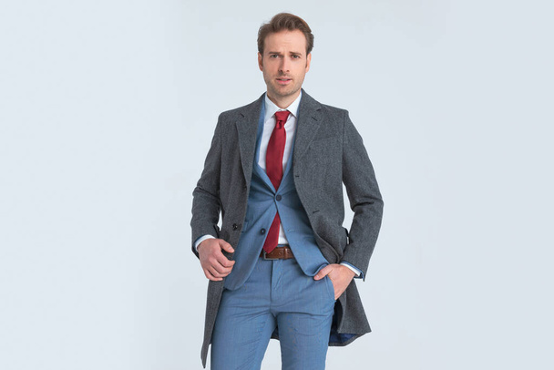 sexy young businessman sticking one hand in pocket, fixing his coat and looking at the camera  - Foto, immagini