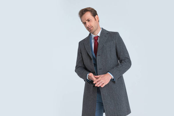 елегантний бізнесмен одягнений у довге пальто, розтирає долоні, дивлячись вниз і драматично
 - Фото, зображення