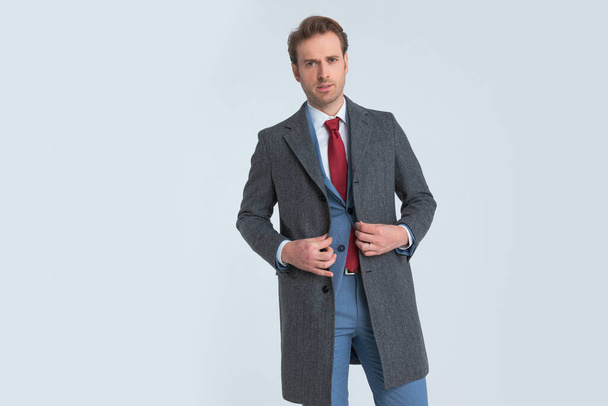 бизнесмен открывает свое длинное пальто, смотрит в камеру и надевает красивый синий костюм - Фото, изображение