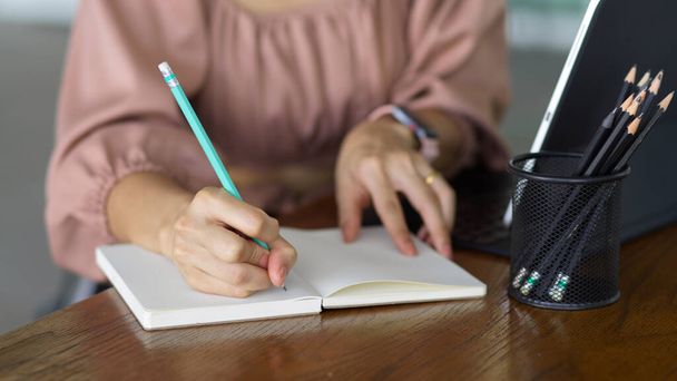 Visão de perto da escrita feminina da mão no notebook enquanto trabalhava com tablet digital na mesa de madeira - Foto, Imagem