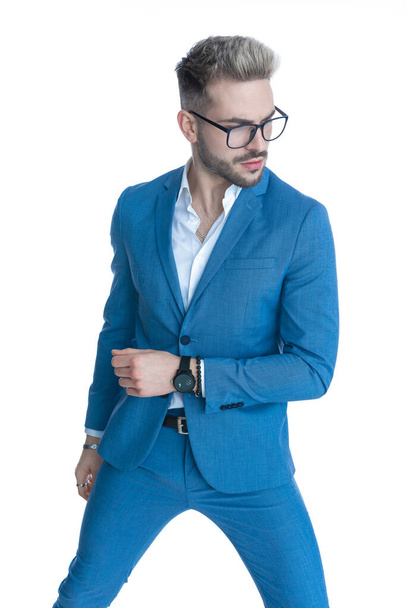 portrait of cool fashion man in blue suit looking to side, holding arm in a fashion pose and confidently posing on white background in studio - Zdjęcie, obraz