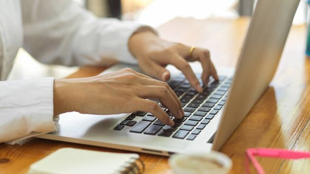 Vista lateral de las manos femeninas escribiendo en el teclado del ordenador portátil en la mesa de madera en la sala de oficina - Foto, Imagen