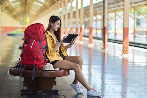 Widok z boku młodej kobiety podróżującej za pomocą tabletu cyfrowego podczas oczekiwania na pociąg na peronie - Zdjęcie, obraz