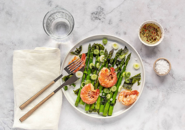 Köstlicher gesunder Salat mit grünem Spargel, Garnelen, Zwiebeln und Nori auf dem weißen Teller. Sauberes Essen. Saisonale Lebensmittel.  - Foto, Bild
