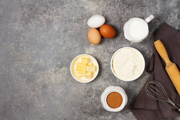 Dough ingredients, milk, eggs, flour and whisk, butter, brown cane sugar, on a gray table, top view, background, no people, horizontal - Photo, Image