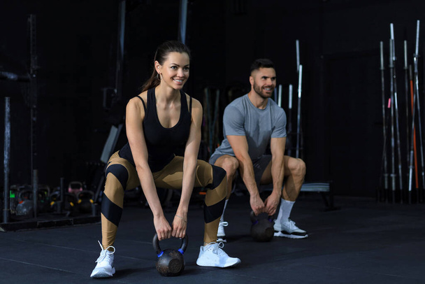 Fit and muscular couple focused on lifting a dumbbell during an exercise class in a gym - Foto, afbeelding