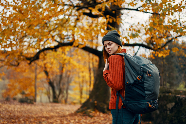 femme en bonnet avec un sac à dos sur la nature dans le paysage forestier et les feuilles tombées - Photo, image