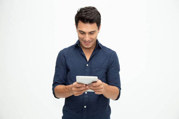 Gelukkige jonge man met behulp van digitale tablet geïsoleerd op witte achtergrond - Foto, afbeelding