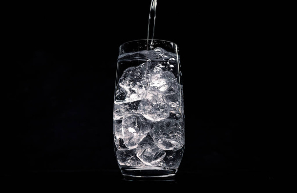 Pouring water in glass with crushed ice on black background with copy space - Photo, Image