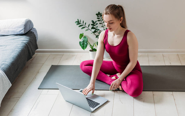Meisje dat thuis yoga beoefent. Vrouw kijkt naar video op het internet en herhaalt de taken. Indoor en outdoor training. Sport en een gezonde actieve levensstijl. - Foto, afbeelding