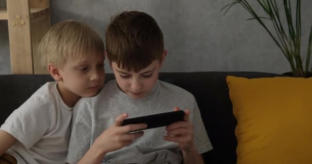 Zwei kleine Jungen spielen auf einem Smartphone und sitzen auf der Couch. Kinder und Spielzeug. Tageslicht - Filmmaterial, Video