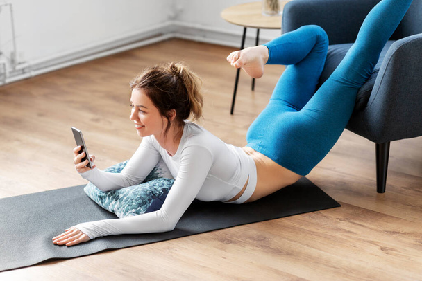 woman with smartphone stretching yoga at home - Fotografie, Obrázek