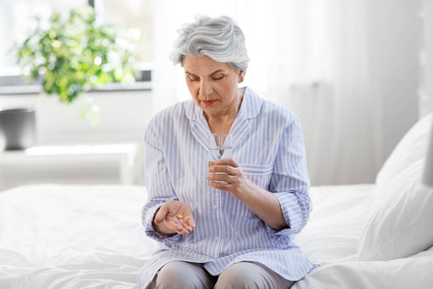 senior woman with pill and water sitting on bed - Φωτογραφία, εικόνα