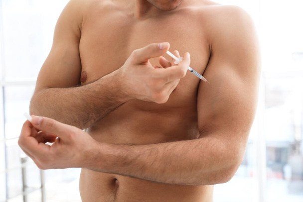 Athletic man injecting himself indoors, closeup. Doping concept - Photo, image