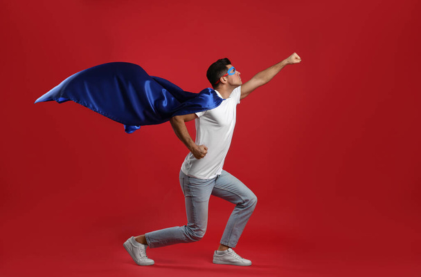 Man wearing superhero cape and mask on red background - Foto, Bild