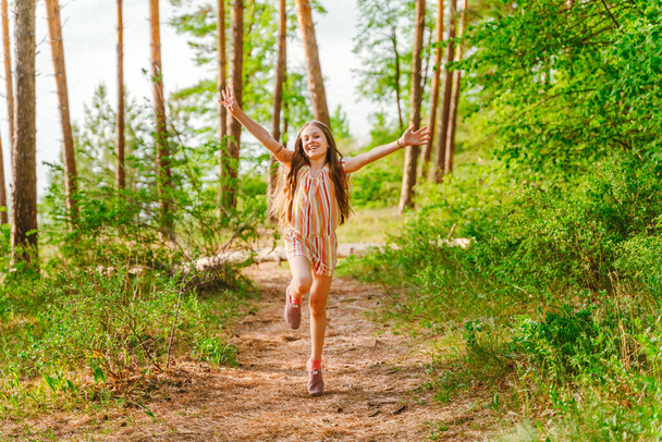 Een klein meisje rent vrolijk met haar armen open op een pad in het bos - Foto, afbeelding