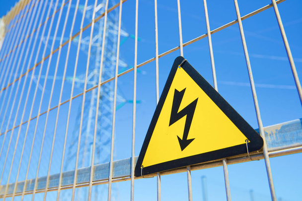 Elektryczny znak zagrożenia umieszczony na metalowym ogrodzeniu. - Zdjęcie, obraz