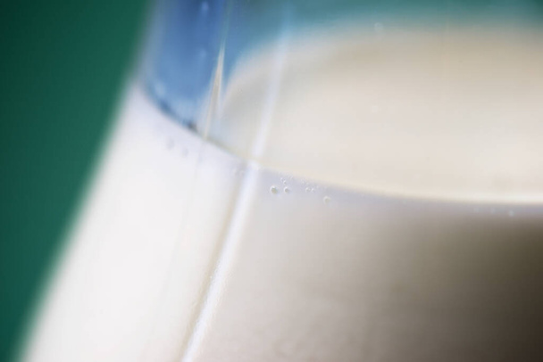 Botella de vidrio llena de leche en una mesa verde. - Foto, Imagen