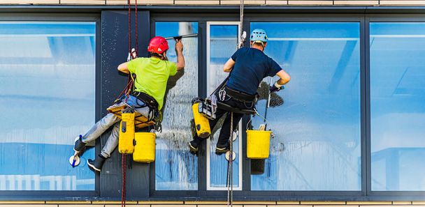 Δύο άντρες καθαρίζουν παράθυρα σε ένα κτίριο γραφείων. - Φωτογραφία, εικόνα