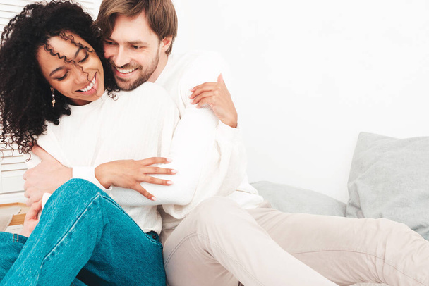 Smiling beautiful woman and her handsome boyfriend. Happy cheerful multiracial family having tender moments. Multiethnic models lying in bed and hugging in white interior. Embracing each other - Foto, imagen