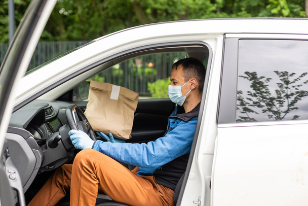 Man by the car. Guy in a delivery uniform. Man in a medical mask. Coronavirus concept. - Photo, Image