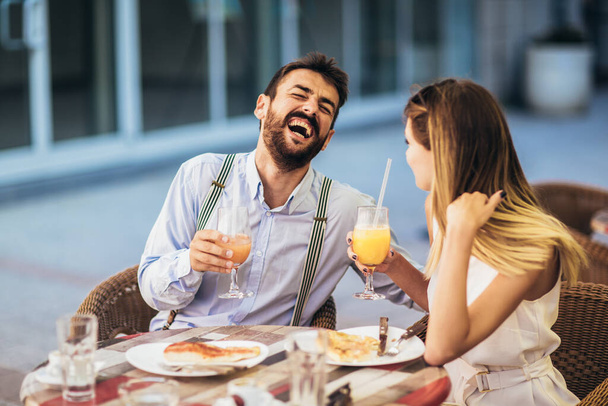 Attraktives und glückliches junges Paar, das sich im Café-Restaurant vergnügt. Sie lächeln und essen eine Pizza. - Foto, Bild